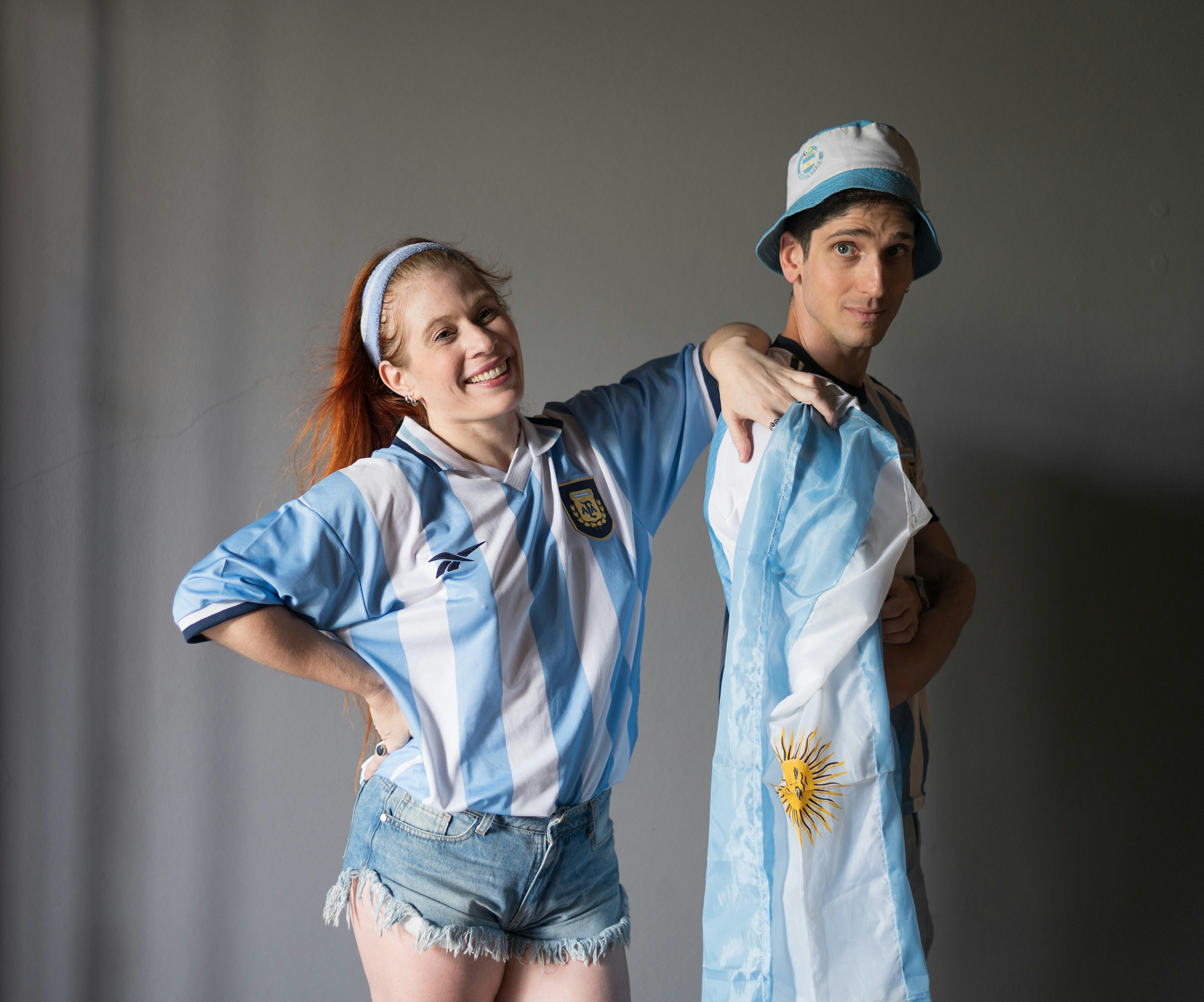 Couple in Argentina jerseys celebrating with national flag indoors.