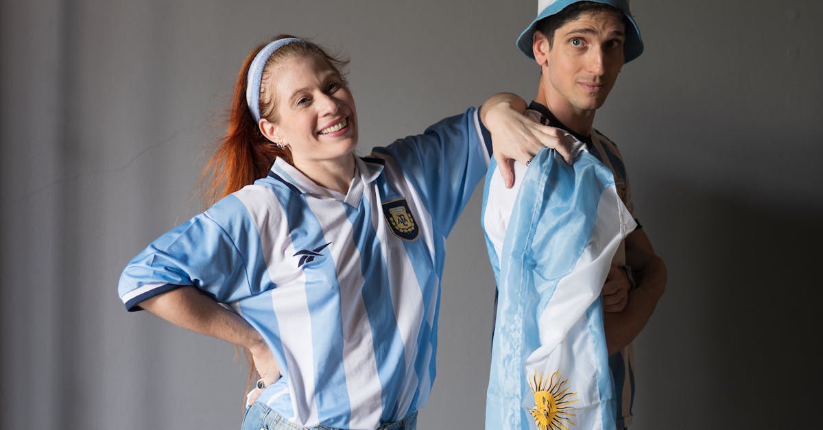 Couple in Argentina jerseys celebrating with national flag indoors.