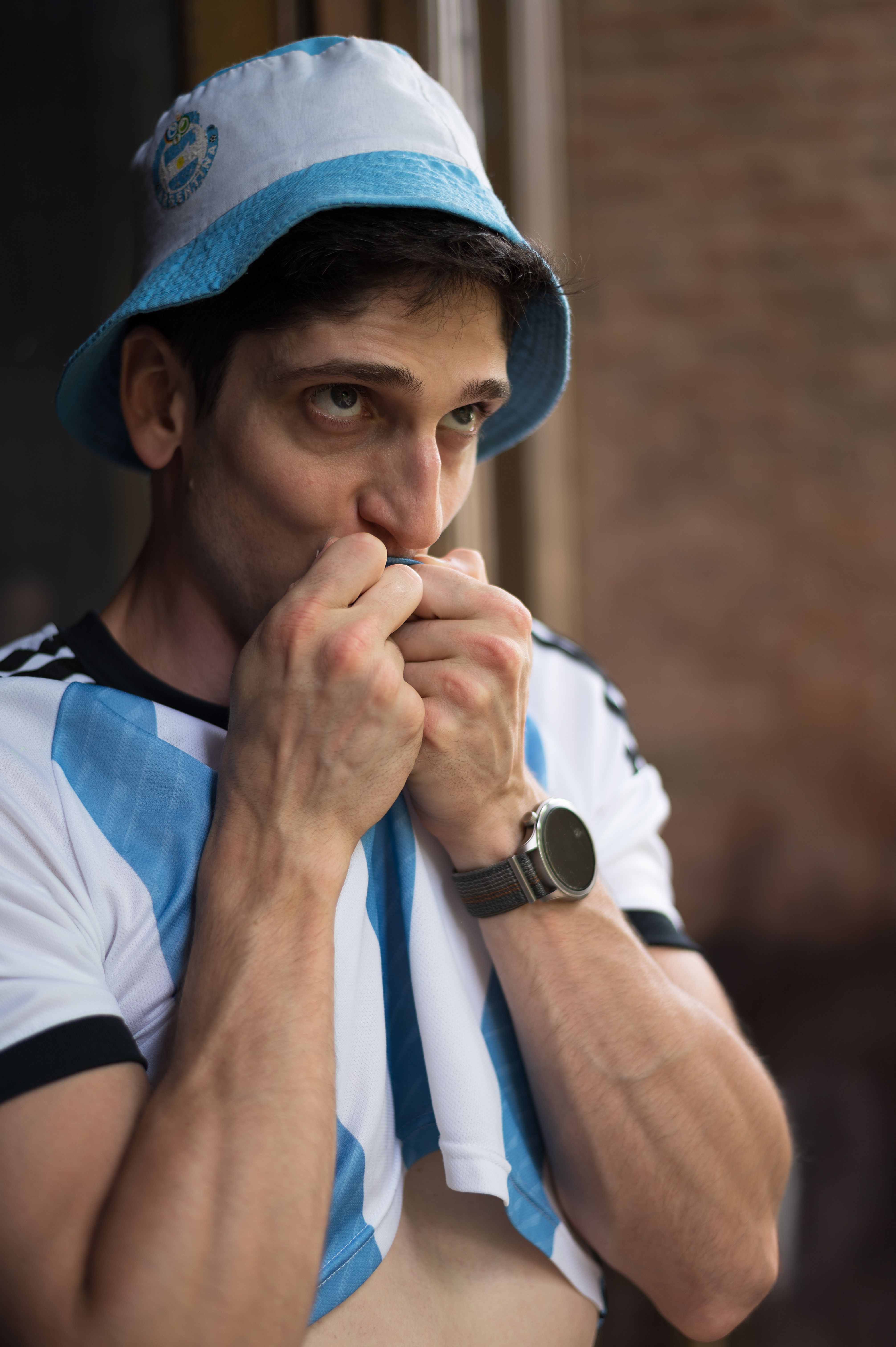 Man wearing Argentina jersey and hat passionately supporting his team indoors.