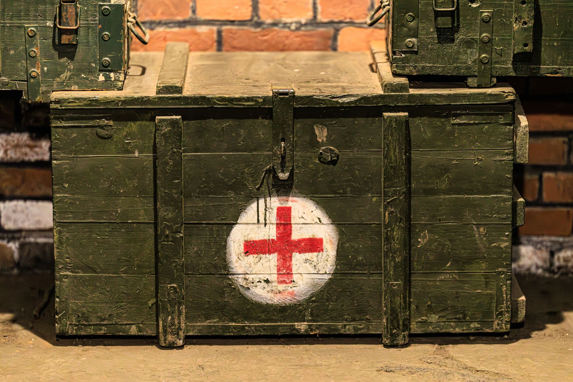 Close-up of a vintage military medical crate with a red cross, set against a rustic brick wall.