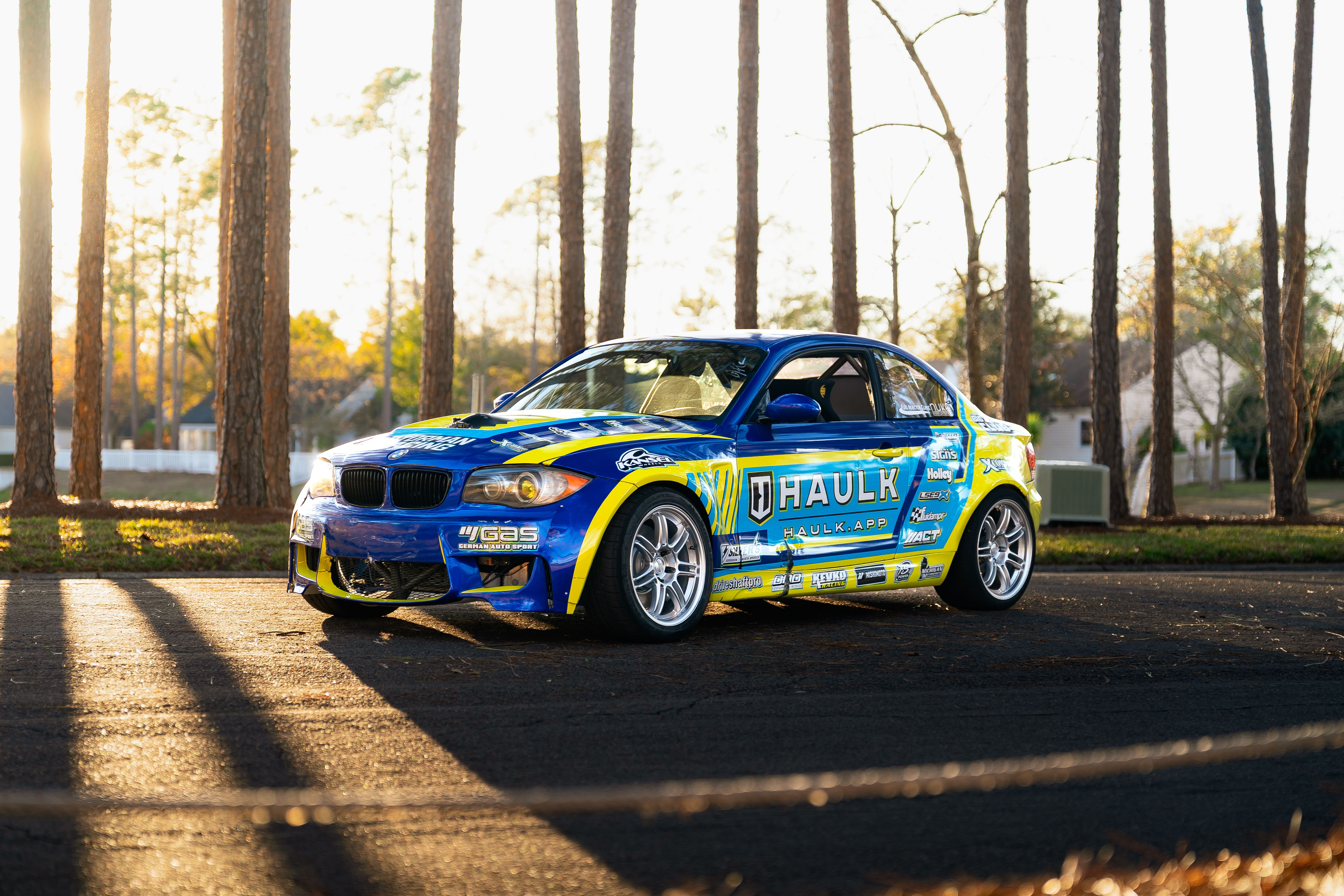 Vibrant Blue Racing Car in Sunlit Pine Forest · Free Stock Photo