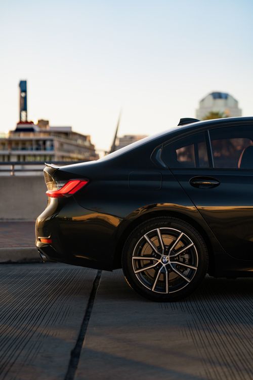Free Side view of a luxury car at sunset with urban buildings in the background, highlighting modern design. Stock Photo
