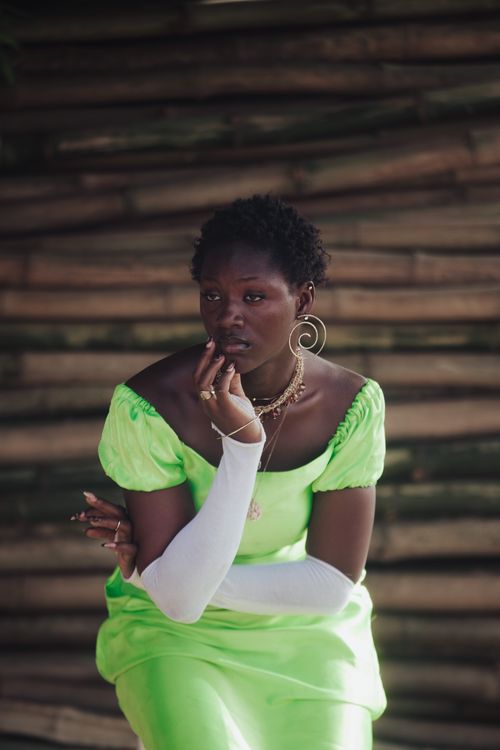 Free Striking portrait of a woman in a neon green dress, with bold accessories, sitting against a wooden background. Stock Photo