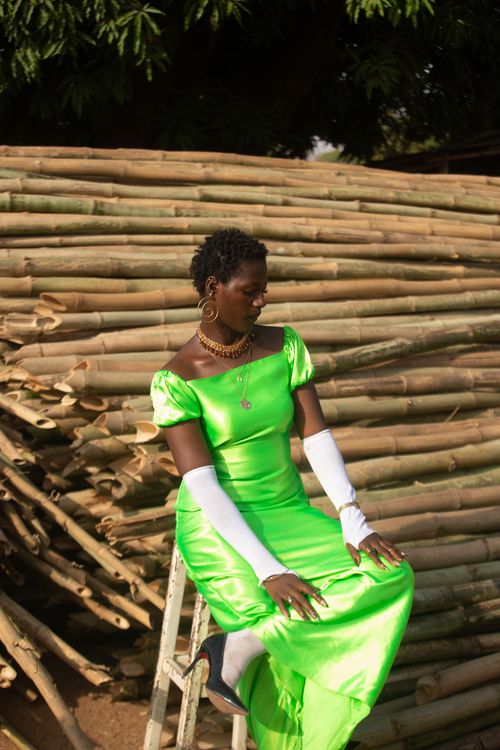 Free Elegant woman in a vibrant green dress sits amidst rustic bamboo, exuding style and poise. Stock Photo