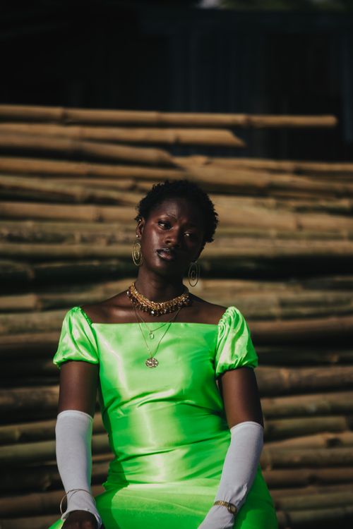 Free Stylish woman posing in a neon green dress against a bamboo backdrop, exuding elegance and modern fashion. Stock Photo