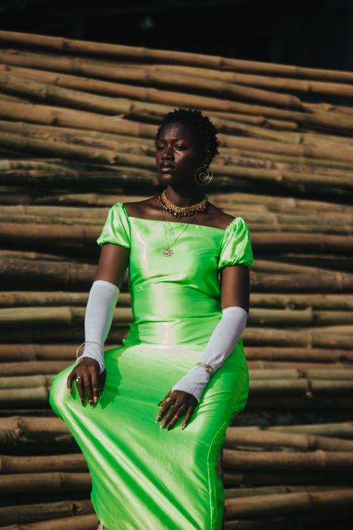 Free African woman in a neon green satin dress posing outdoors against bamboo. Stock Photo