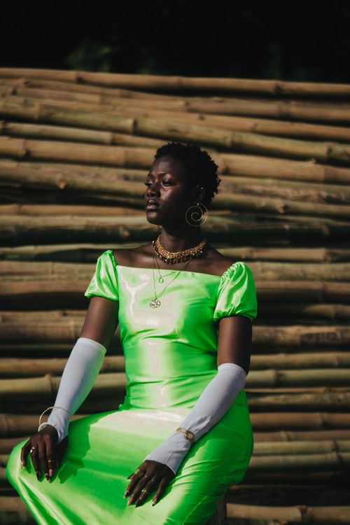Free Stylish woman in a vibrant green dress sitting against a bamboo background, exuding elegance and confidence. Stock Photo