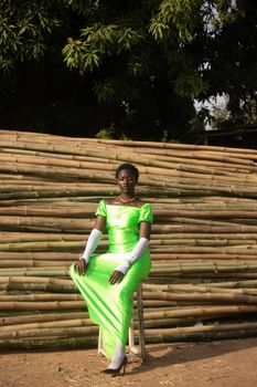 Woman in a bright green dress sits gracefully outdoors against a bamboo backdrop.
