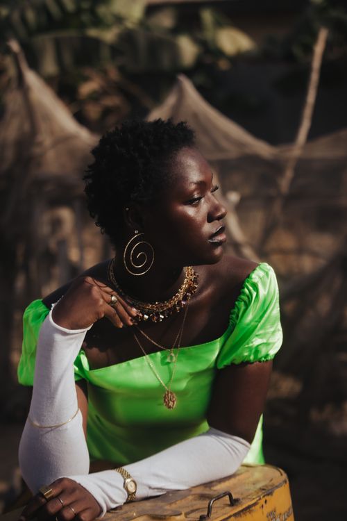 Free Elegant portrait of a woman in a vibrant green dress, adorned with statement jewelry, set in a natural outdoor environment. Stock Photo