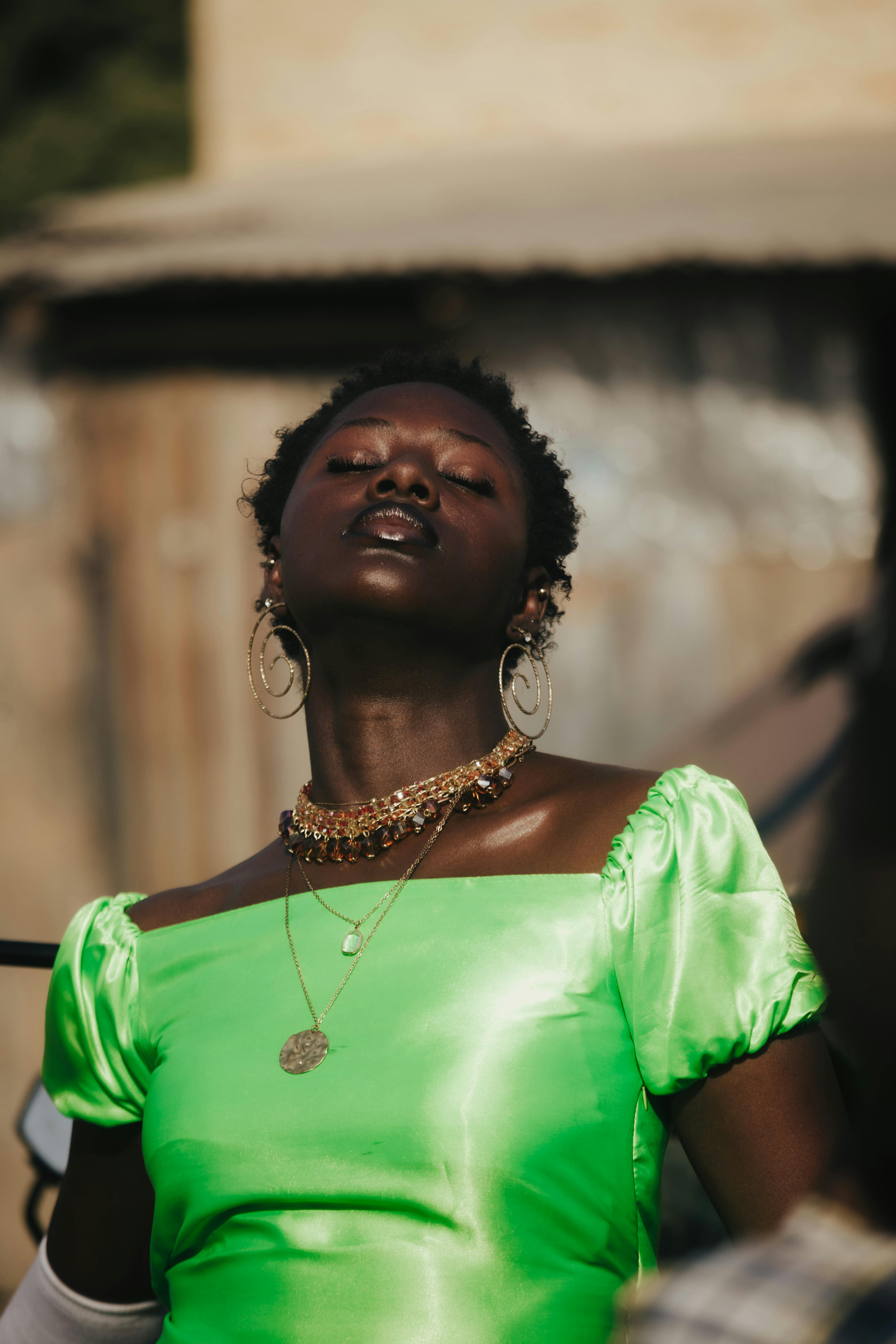 Free A fashionable woman in a vibrant green dress, adorned with statement jewelry, posing confidently outdoors. Stock Photo