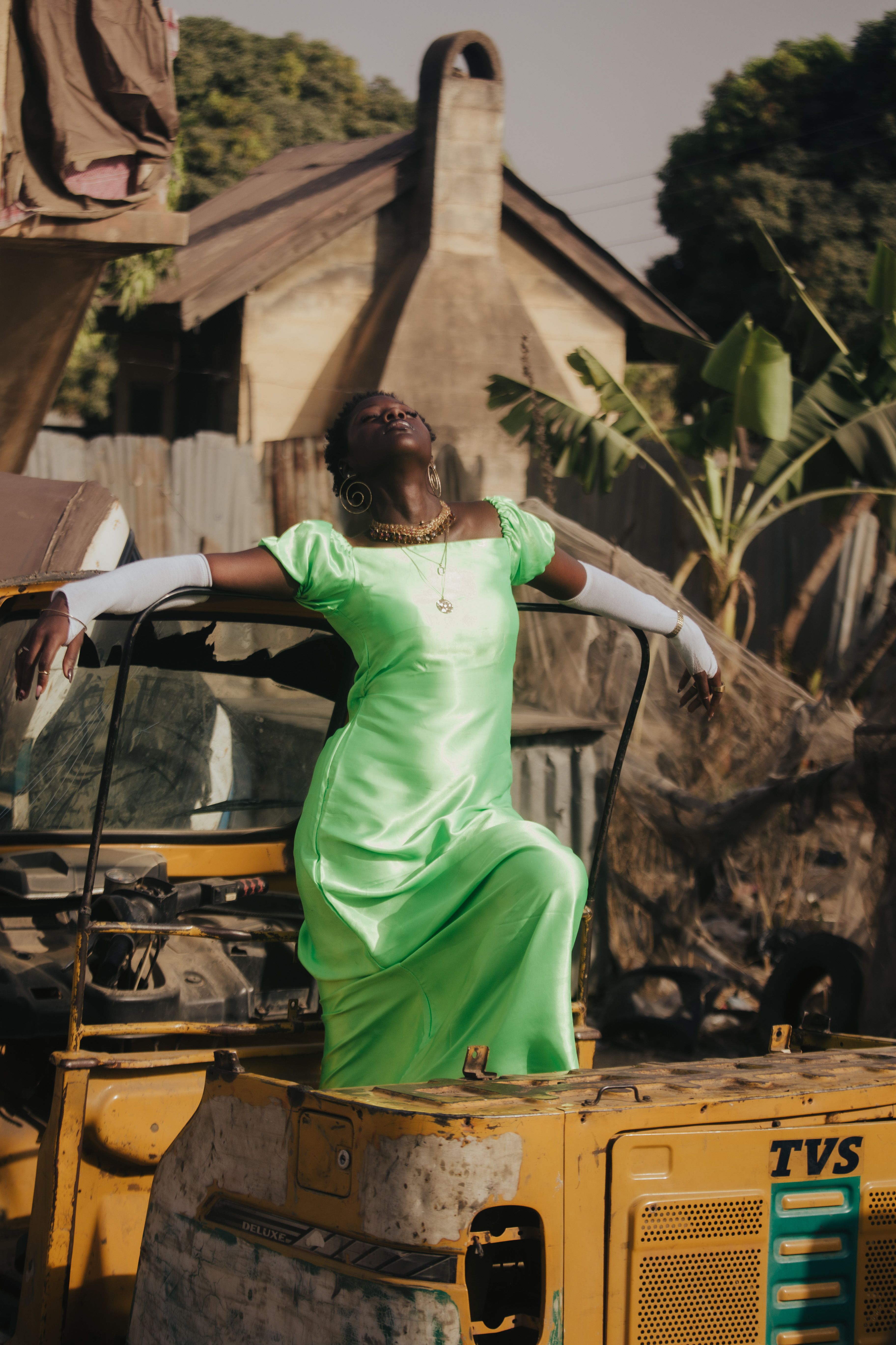 Woman in elegant green dress poses atop machinery in a rustic outdoor setting.