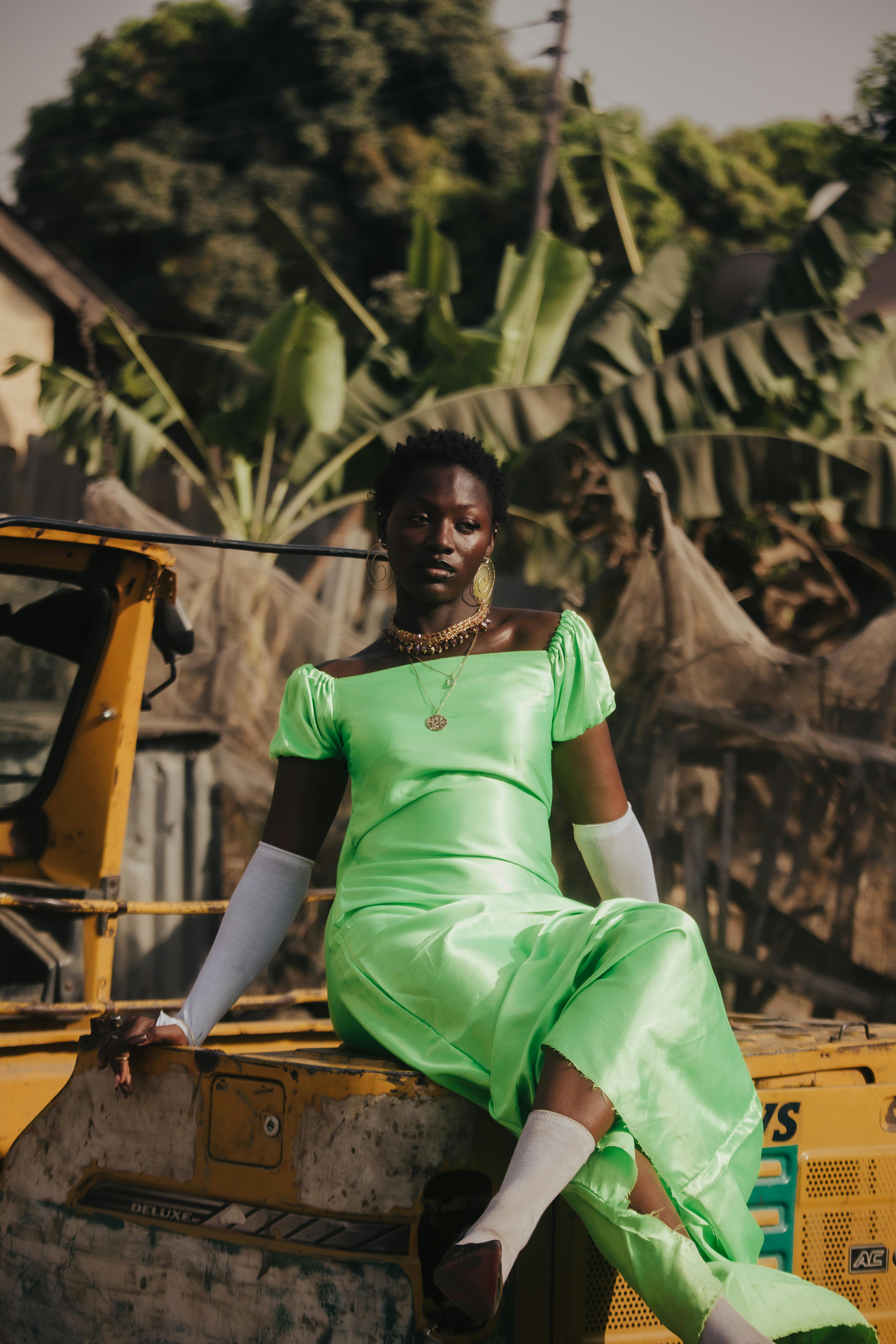 Stylish woman in a bright green dress poses outdoors on a sunny day with tropical plants.