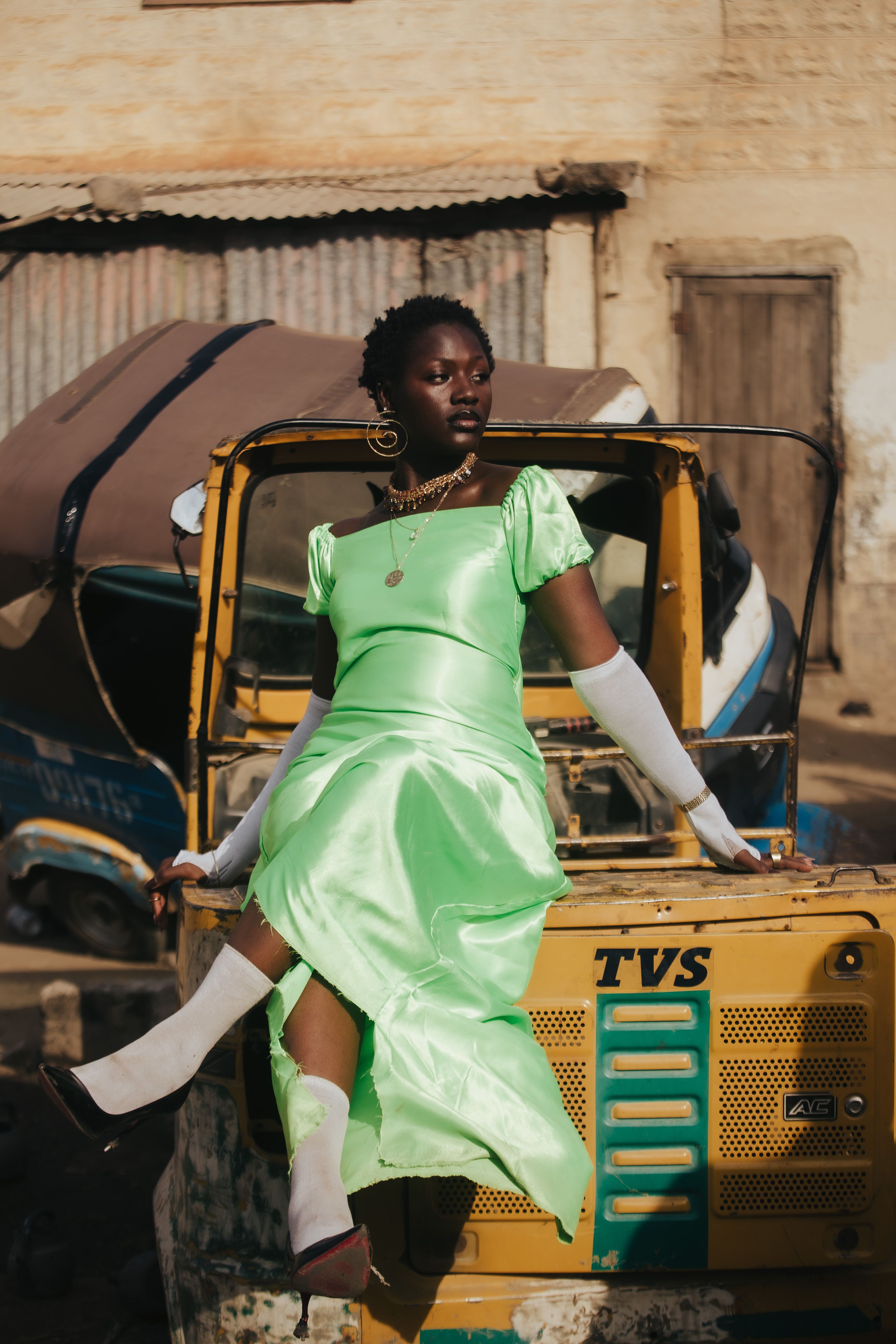 Stylish woman in a vibrant green dress posing on a tuk-tuk in an urban setting.