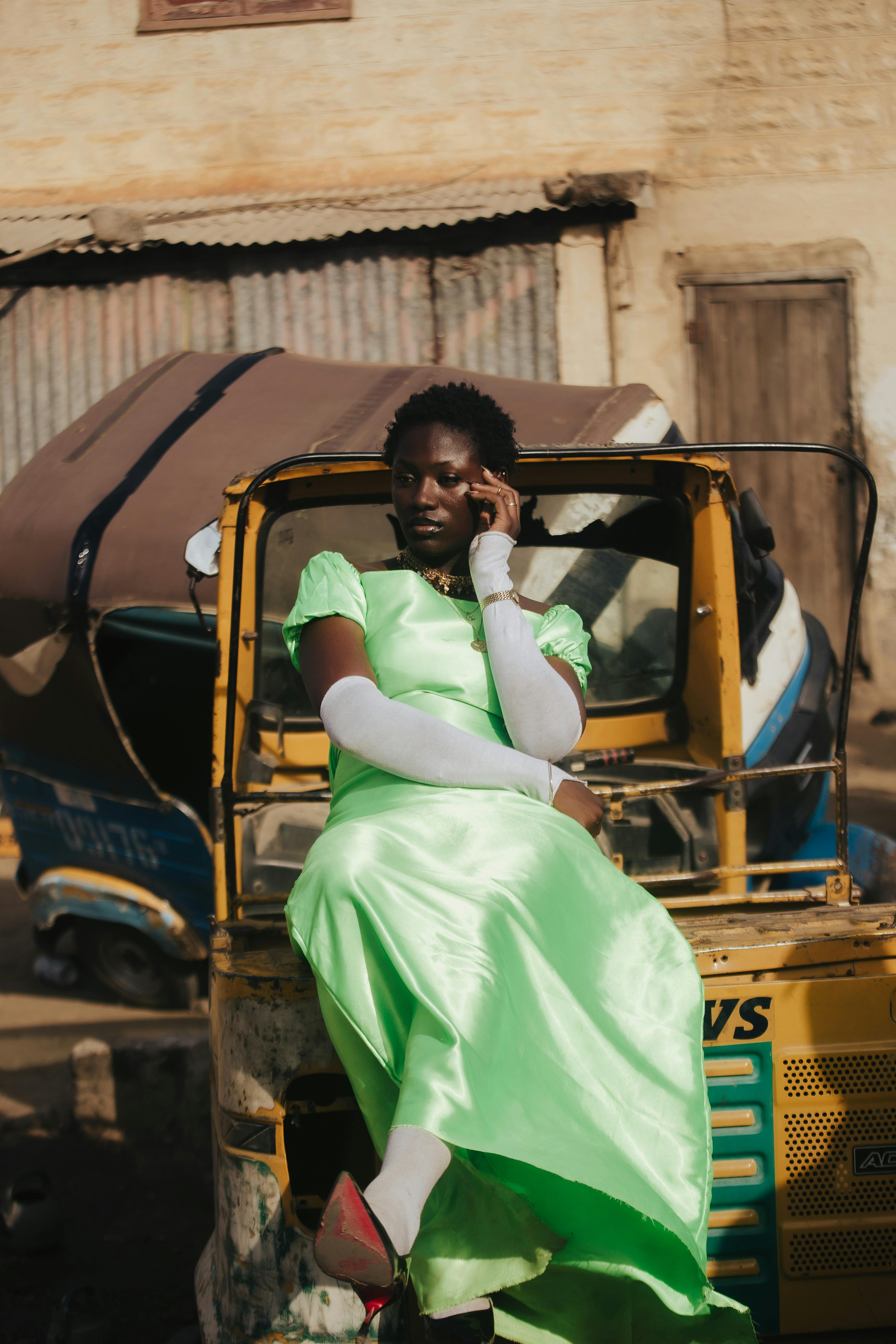 A fashionable woman in a bright dress sits on a rickshaw in an urban outdoor setting, radiating confidence.
