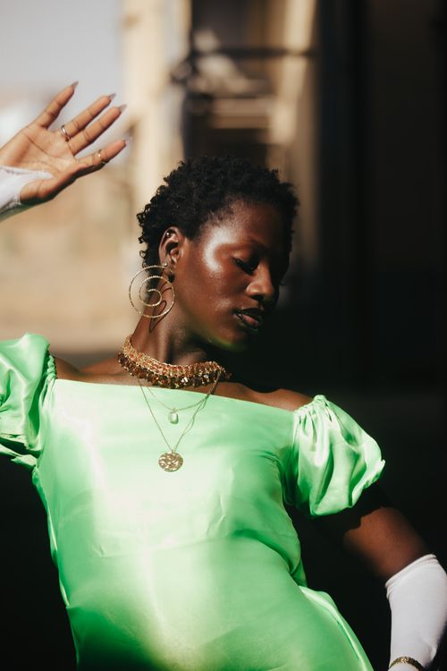 Free Elegant portrait of a woman in a green dress with bold accessories, exuding confidence. Stock Photo