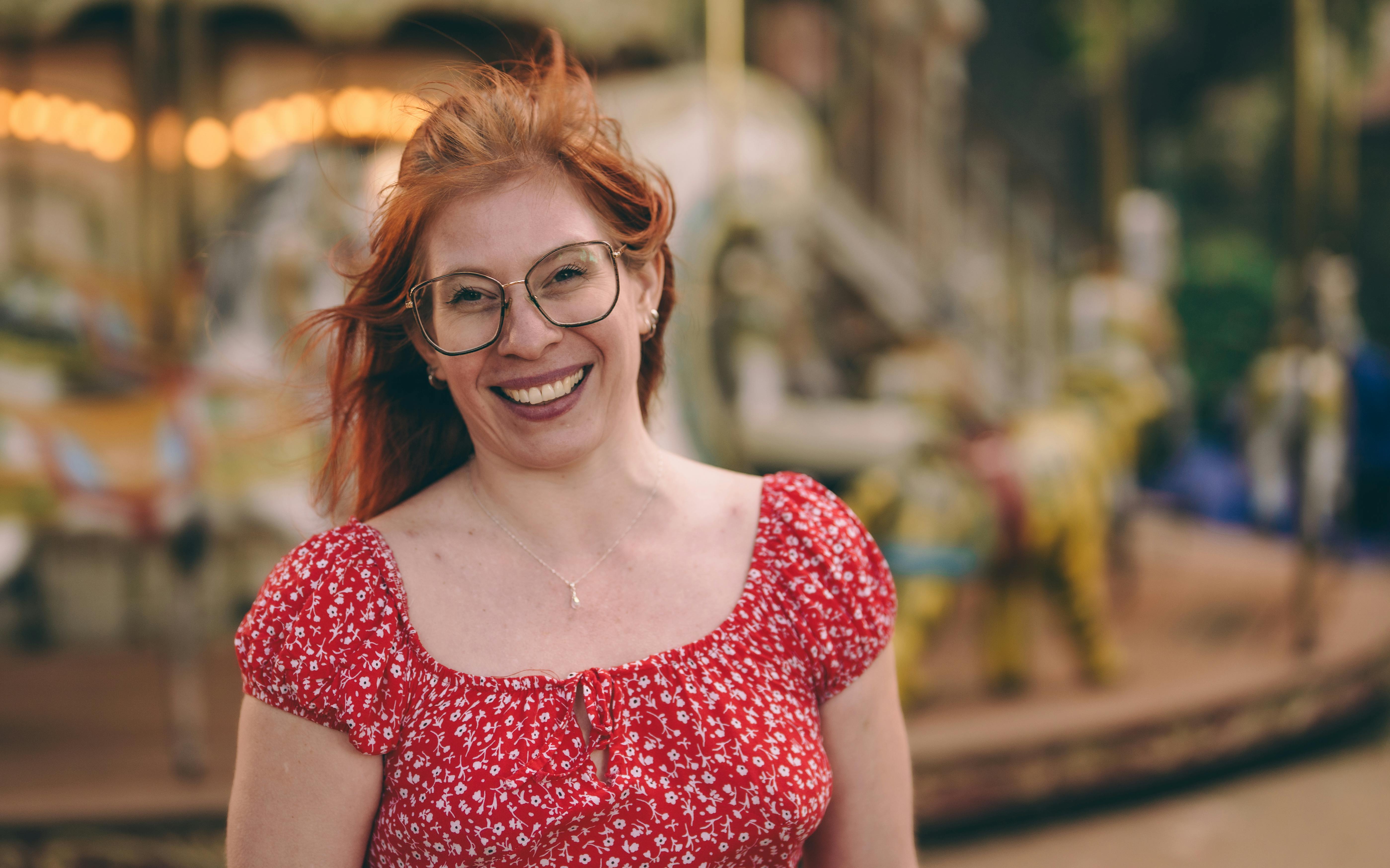 Free Woman wearing red floral dress smiling in front of carousel outdoors. Stock Photo