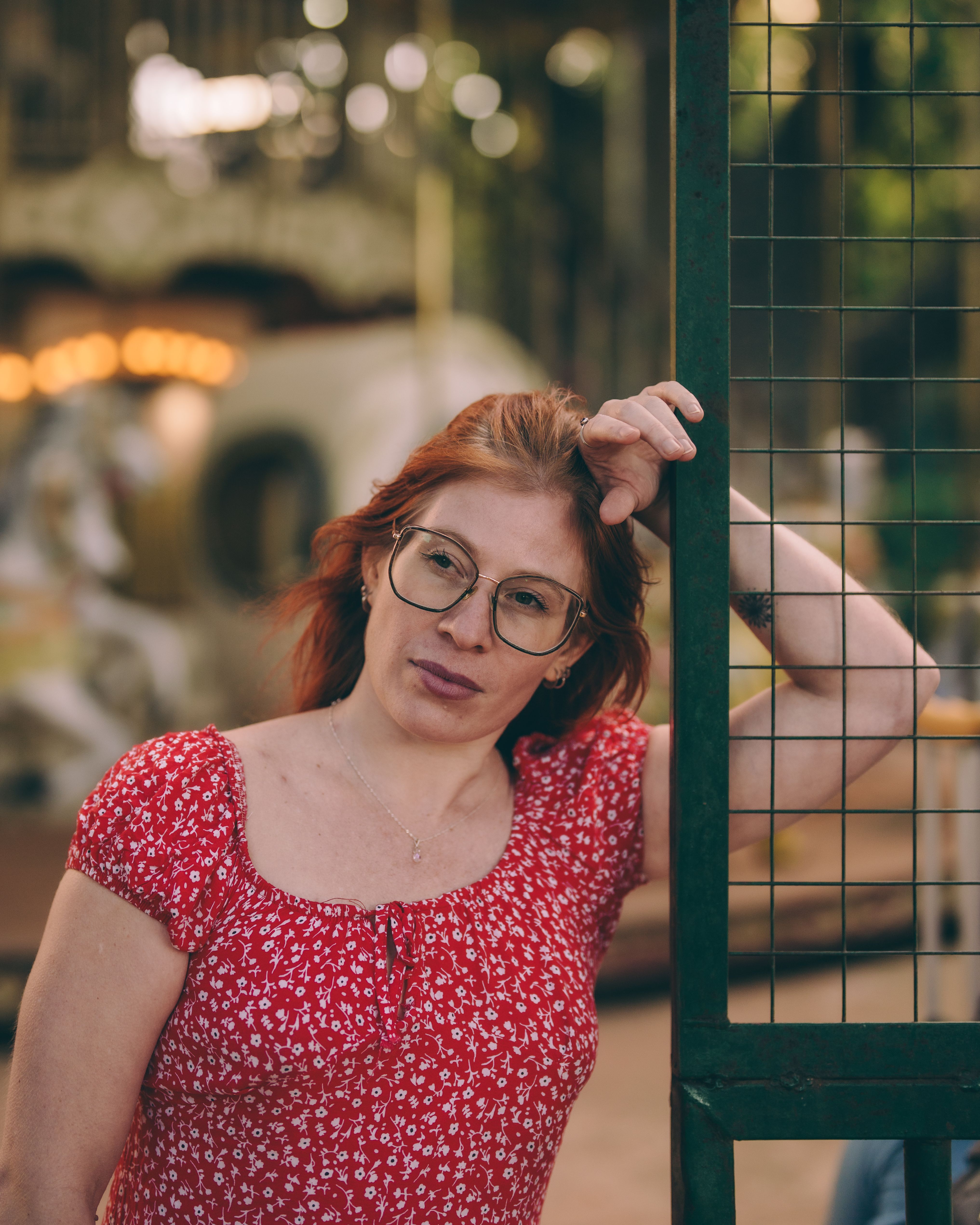 Adult woman in red dress leaning on a fence near a carousel. Calm and serene atmosphere.