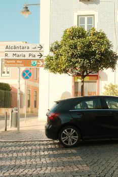 Charming Lisbon street with directional signs, tree, and parked car under daylight.