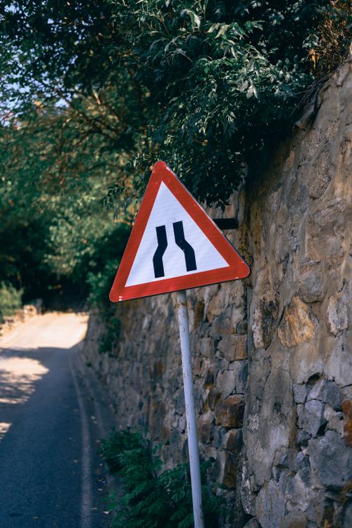 Free Triangular traffic sign indicating road narrowing on a scenic mountain path. Stock Photo