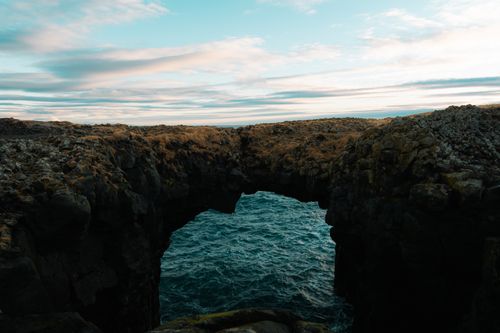Free Stunning view of a natural rock arch over the ocean in Iceland, showcasing rugged beauty and dramatic skies. Stock Photo