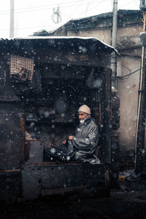 Free Elderly man in a cozy workshop surrounded by falling snow, creating a serene winter scene. Stock Photo