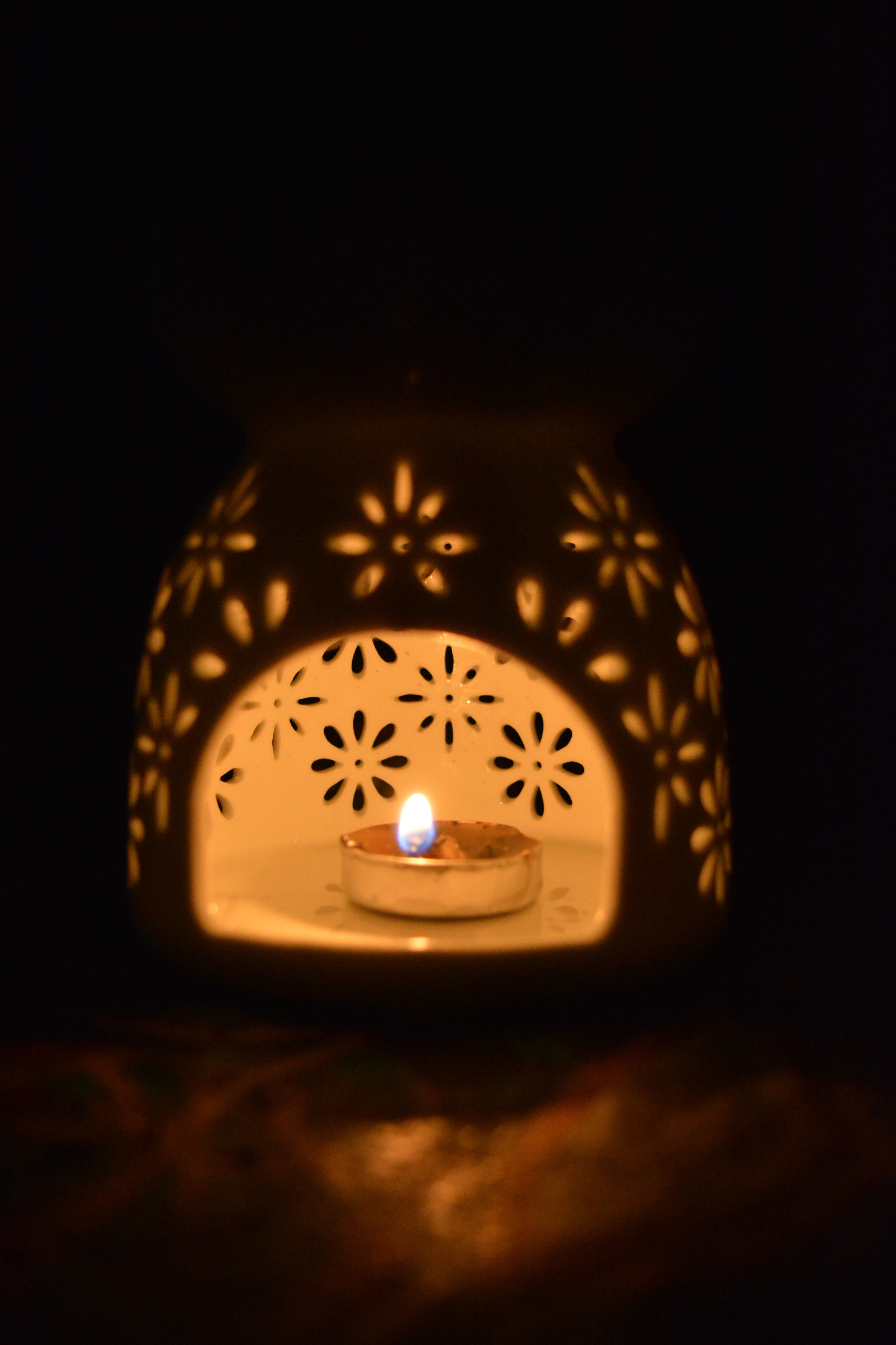 A glowing candle inside an artistic floral ceramic oil burner creates a meditative ambiance.