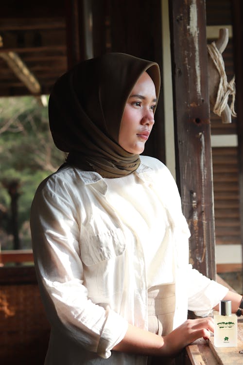 Zdjęcie Stojącej Kobiety W Białej Koszuli Z Długim Rękawem I Brązowym Hidżabu, Patrząc W Dal