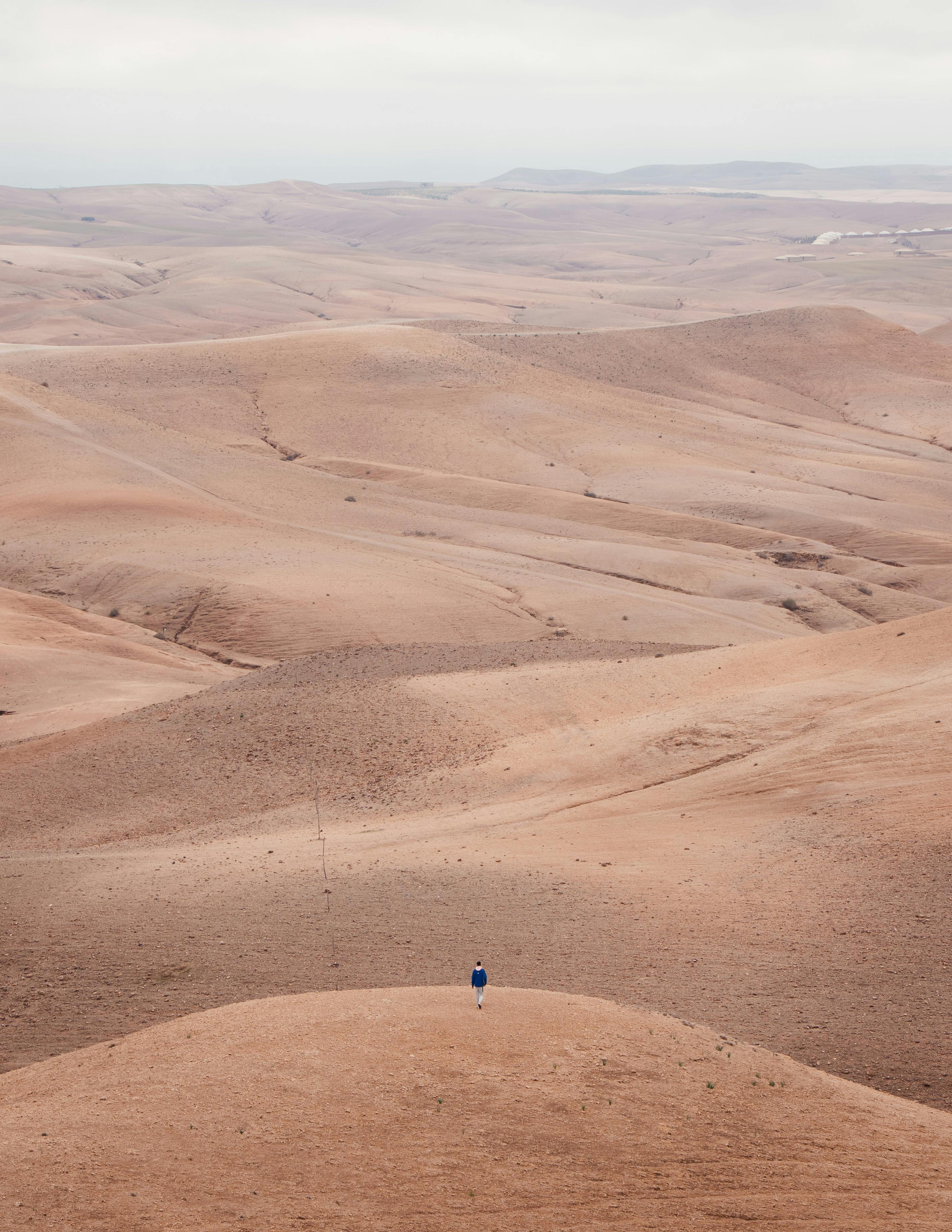 Free Solitary person standing in the vast, rolling Agafay Desert, Morocco under a cloudy sky. Stock Photo