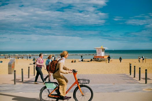 People enjoying a sunny day at the beach in Barcelona, with a cyclist in the foreground.