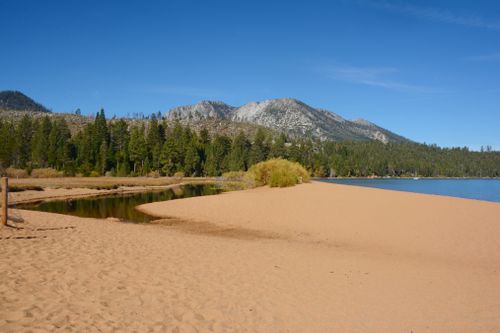 Free Picturesque view of South Lake Tahoe with sandy beach, evergreen trees, and Sierra Nevada mountains. Stock Photo
