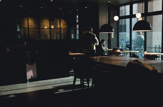 Warm urban cafe interior with people relaxing, enjoying an afternoon. Soft lighting and modern decor create a cozy atmosphere.