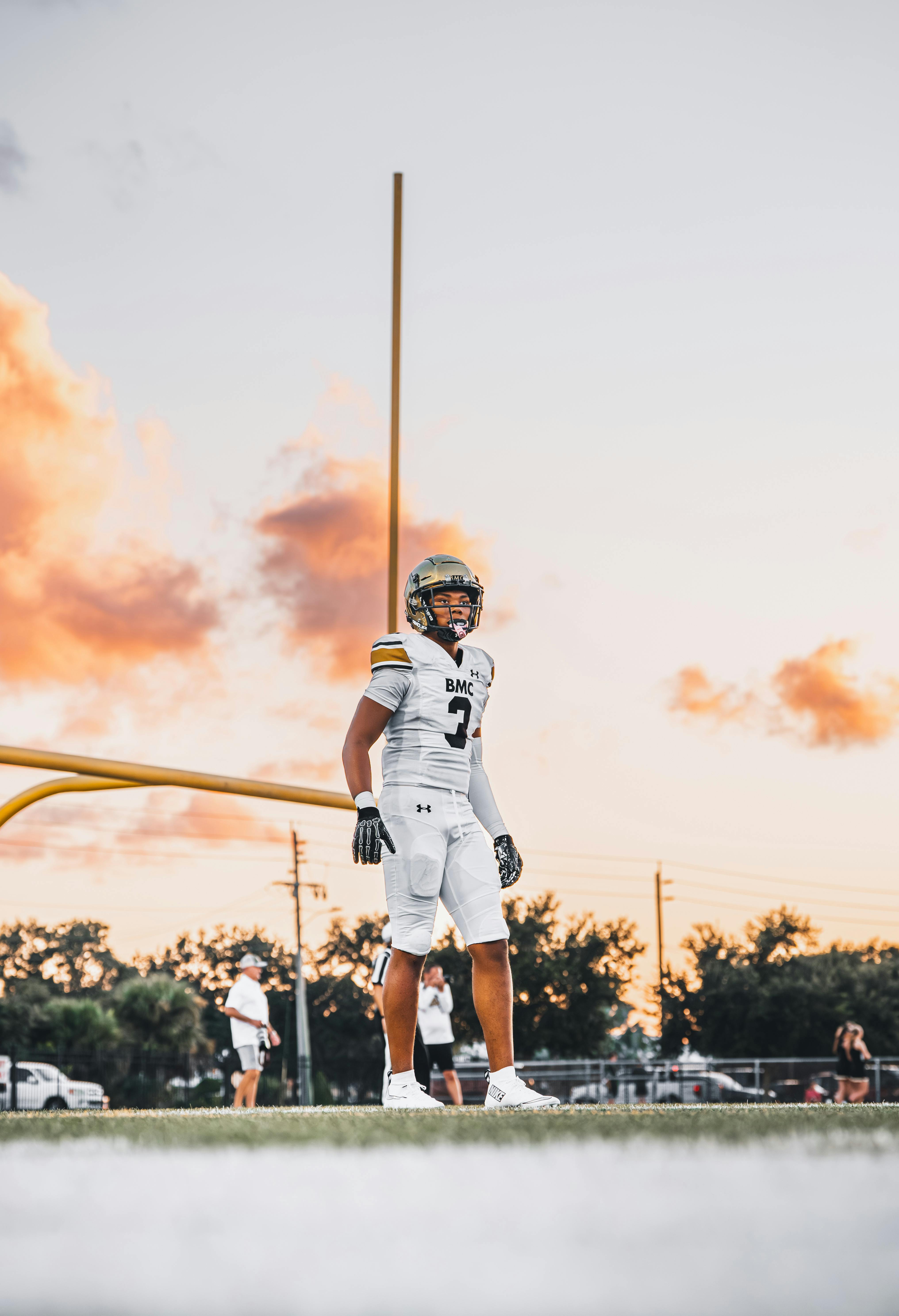 A young American football player stands confidently on the field at sunset, creating a dramatic athletic scene.