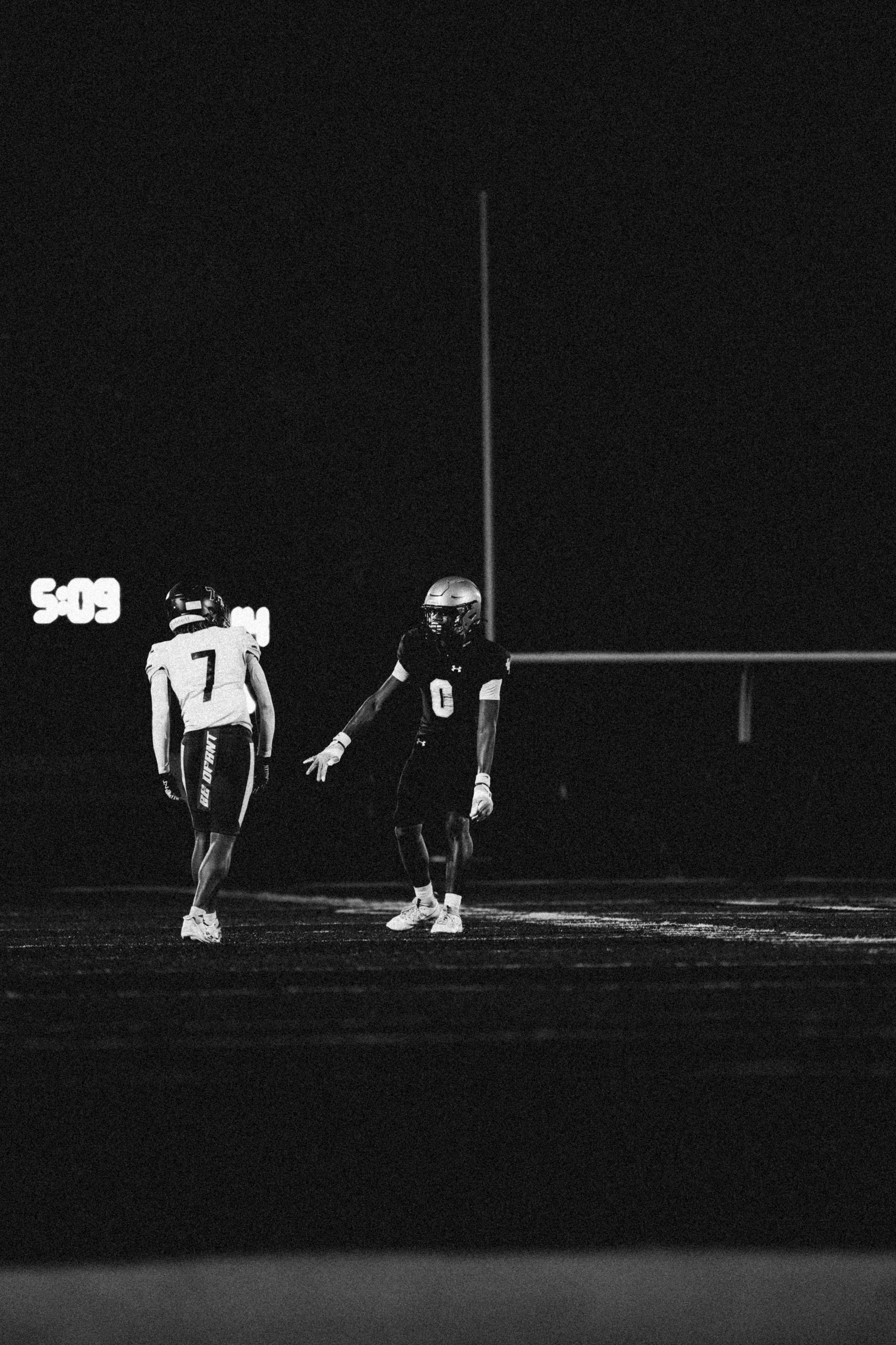 A dynamic black and white photo capturing a night football game with players in motion.