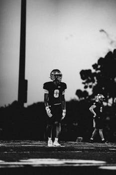 A black and white image of a football player standing on a field in the evening light with a moody atmosphere.