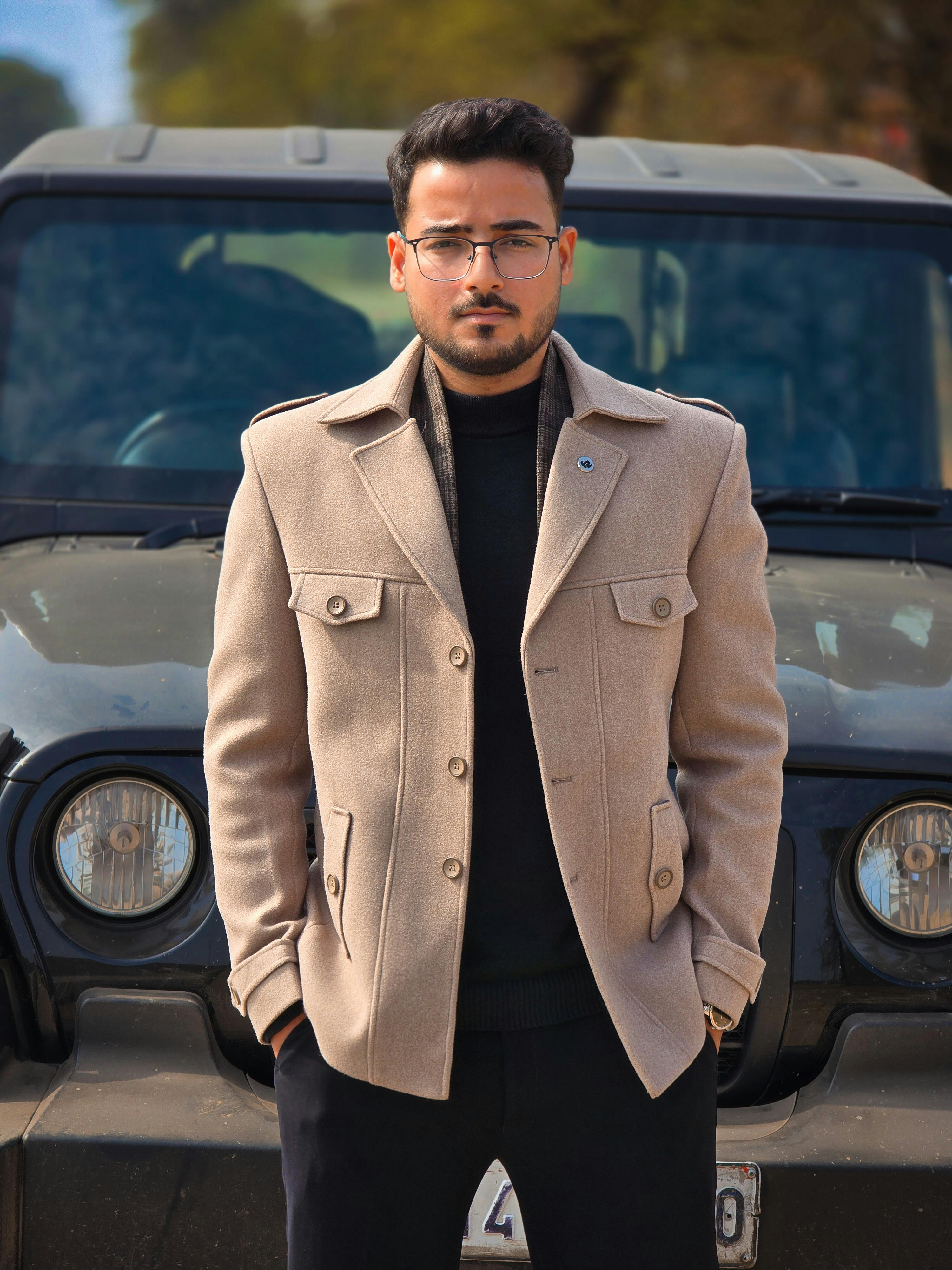 Fashionable man in beige coat standing in front of a jeep outdoors.