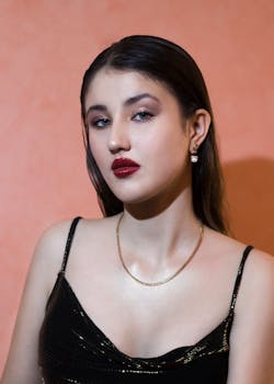 这幅肖像画优雅地描绘了一位女性，她身着黑色上衣，红唇引人注目，在温暖的背景下摆出姿势