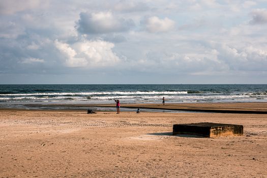 A tranquil beach with people enjoying the evening shore and a concrete block in the foreground.