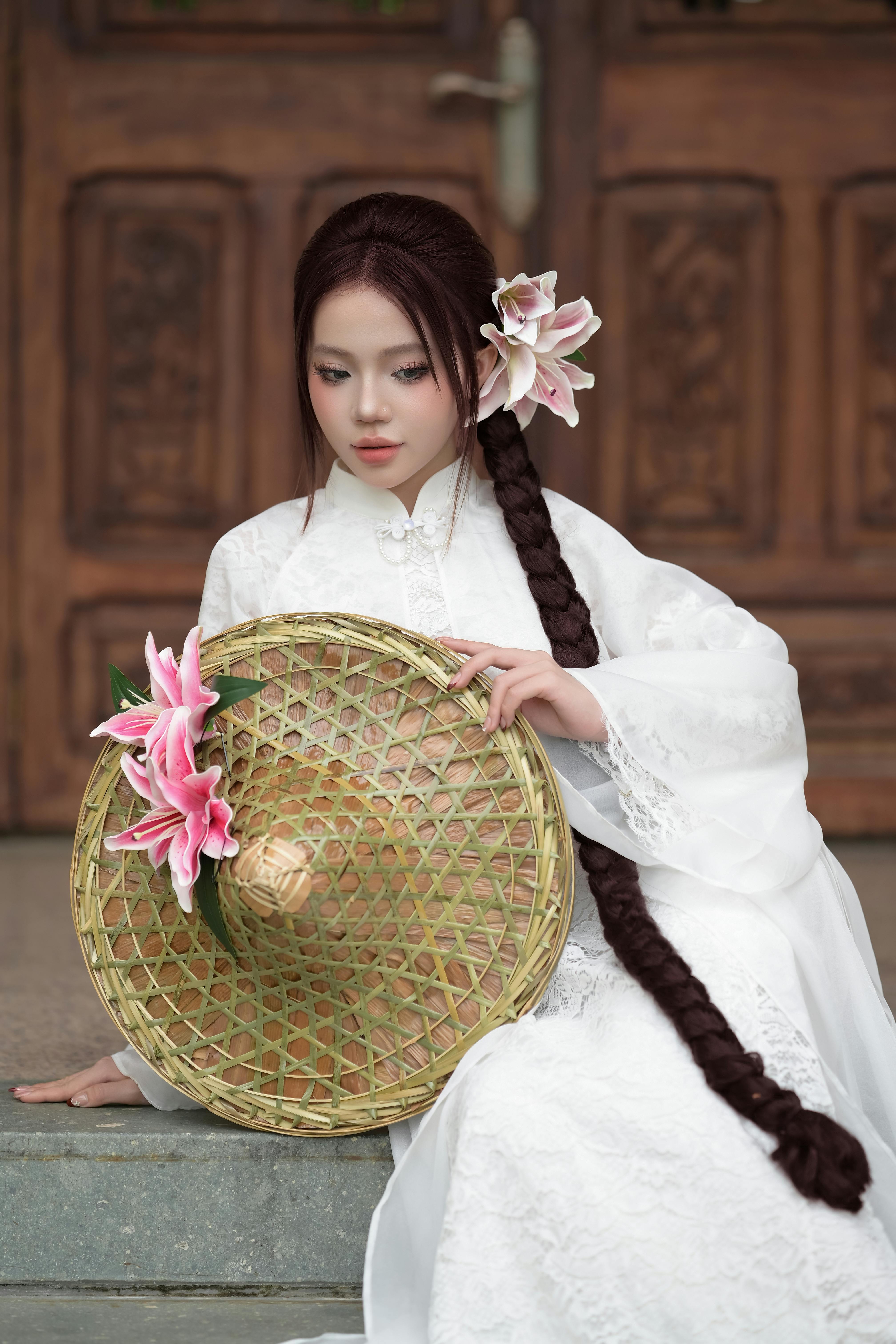 Asian woman in traditional white dress with braided hair and lily flowers.