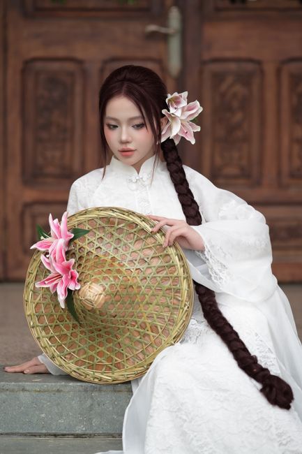 Asian woman in traditional white dress with braided hair and lily flowers.