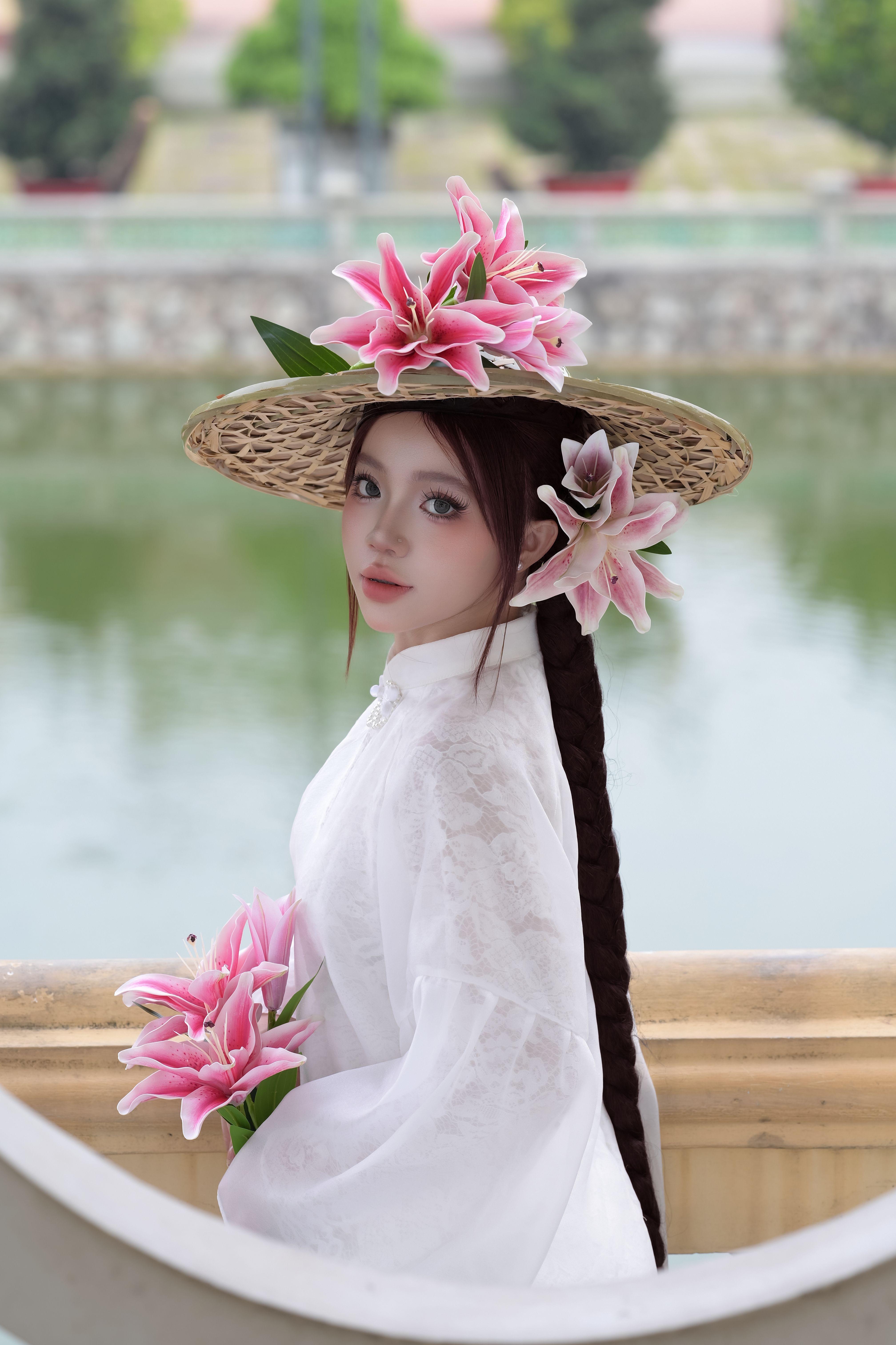 A woman in traditional white attire poses elegantly outdoors with floral accessories.
