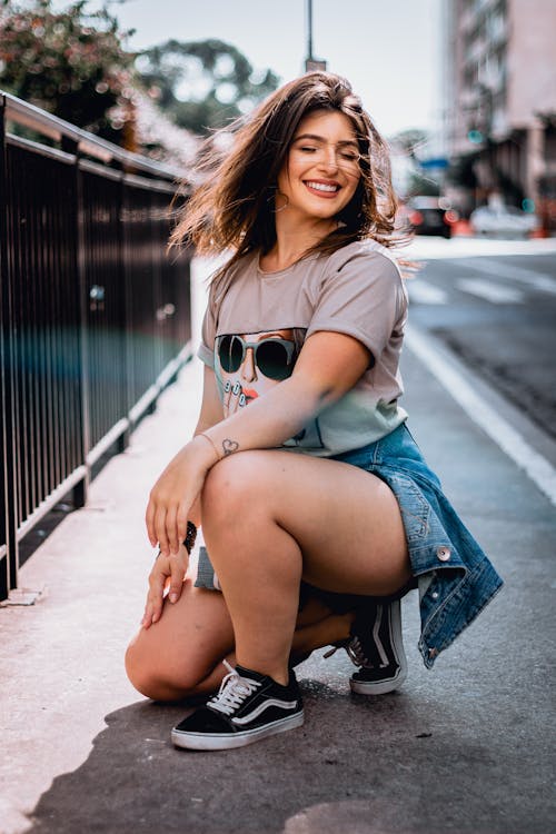 grátis Foto De Foco Seletivo De Mulher Sorridente Ajoelhada Ao Lado Da Estrada Enquanto Posa Com Os Olhos Fechados Foto profissional