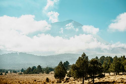 Free Serene view of a mountain surrounded by lush forest and clouds under a clear blue sky. Stock Photo