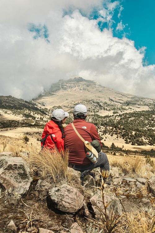 Free A couple sits on rocky terrain, admiring the vast mountain landscape. Stock Photo