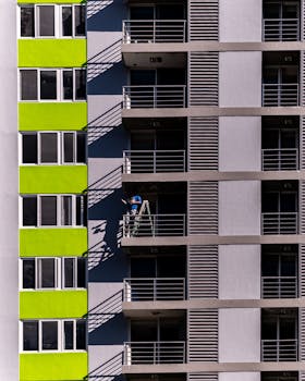 一张现代建筑的特写图像，阳台上有一名工人在梯子上