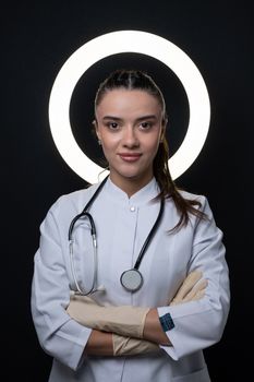 Portrait of a confident female doctor in a white coat with a stethoscope, standing indoors.