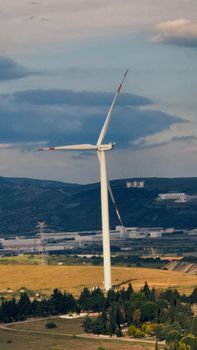 A wind turbine stands tall in a rural setting with hills and a blue sky.