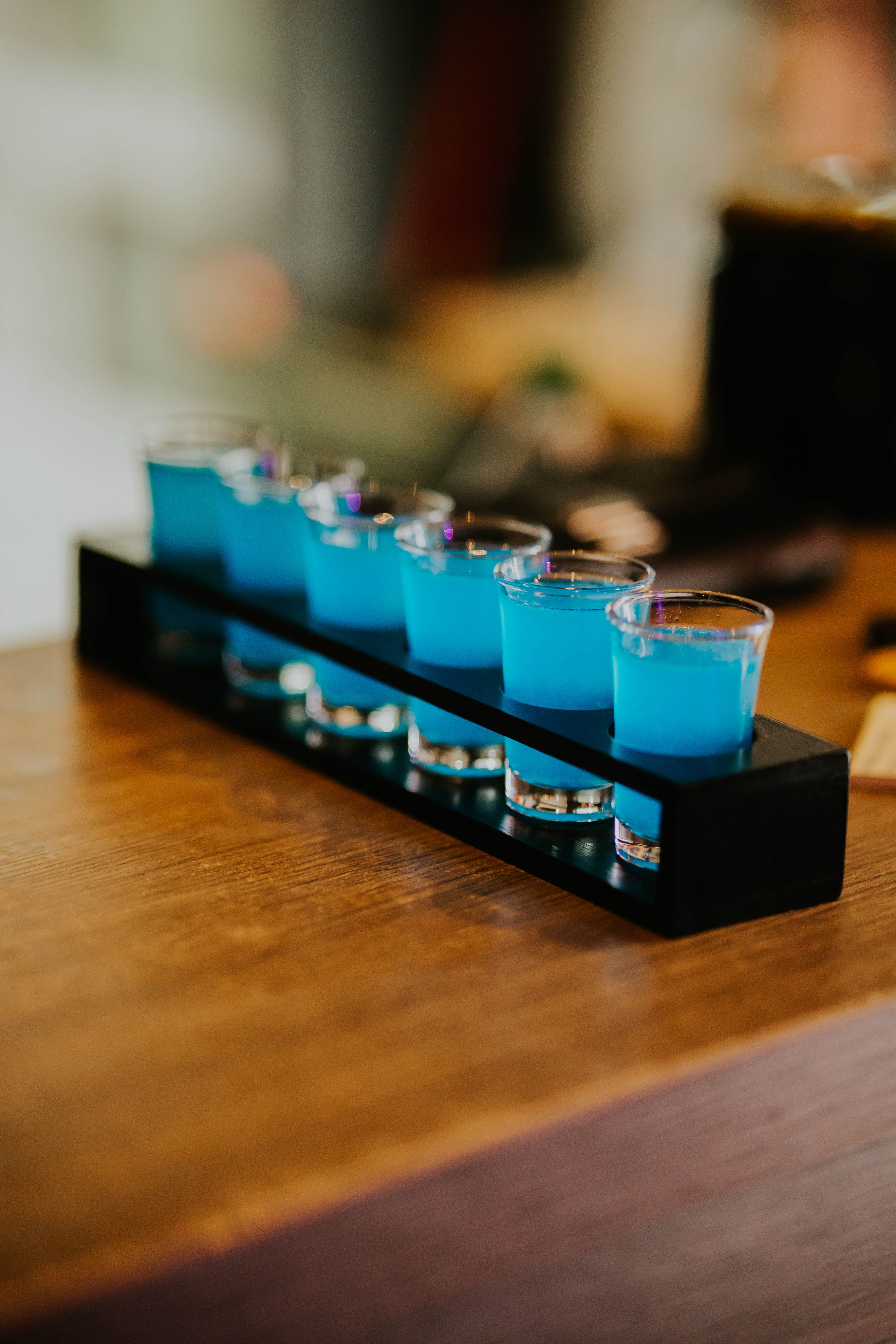 Close-up of vibrant blue cocktails in shot glasses on a stylish wooden bar surface.
