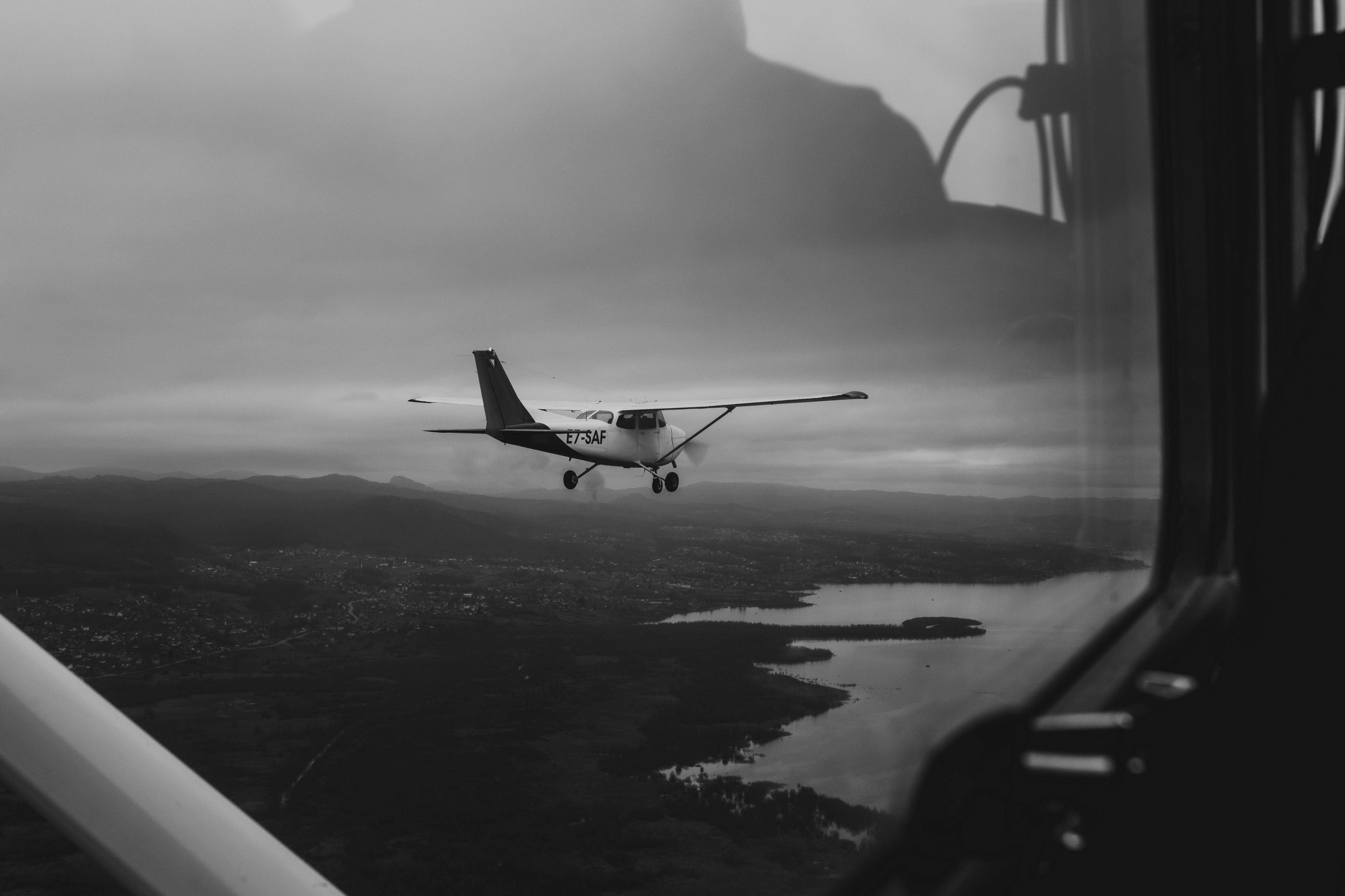 бесплатная Черно-белая аэрофотография, на которой запечатлен небольшой самолет, летящий над обширным ландшафтом под облачным небом. Стоковое фото