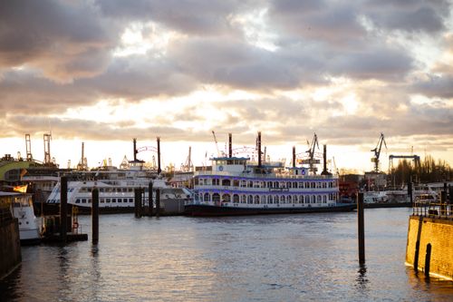 Free A scenic view of Hamburg's port at sunset, showcasing a historic paddle steamer and modern harbor cranes. Stock Photo