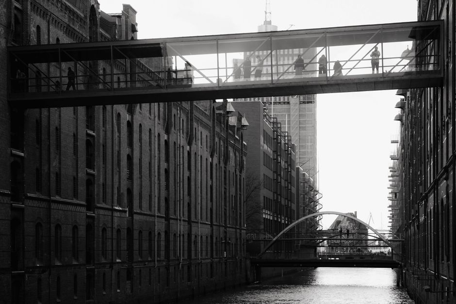 Black and white view of pedestrians on a bridge in Hamburg's Speicherstadt with canal below.